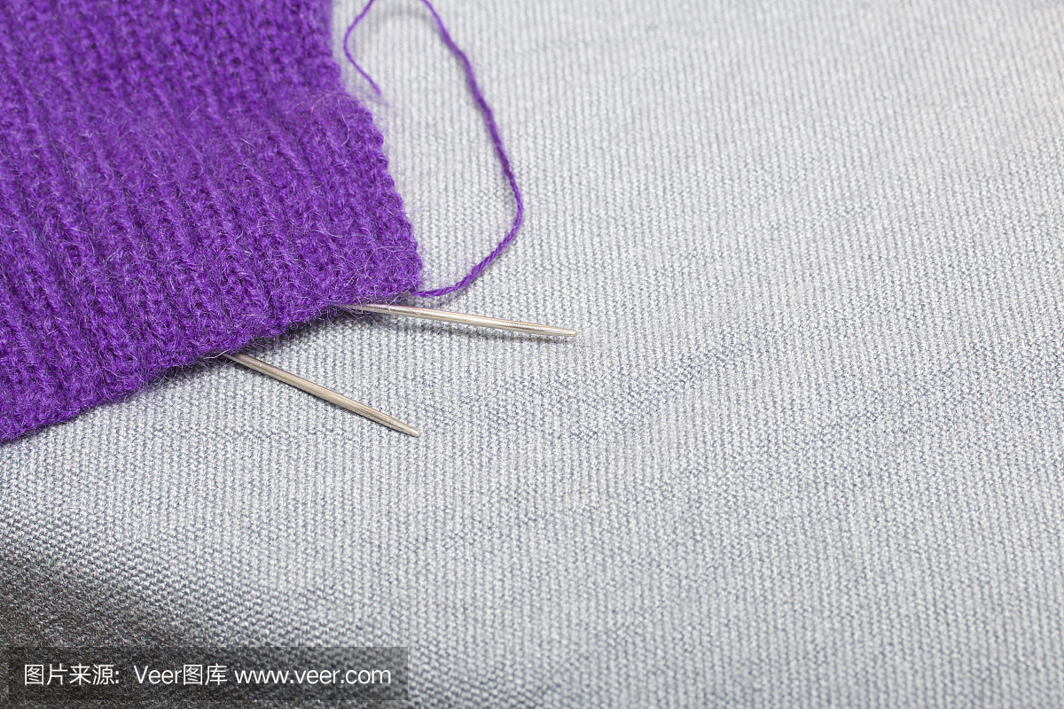用钢针编织。在未完成的编织中由紫色的线和钢编织针组成的球。